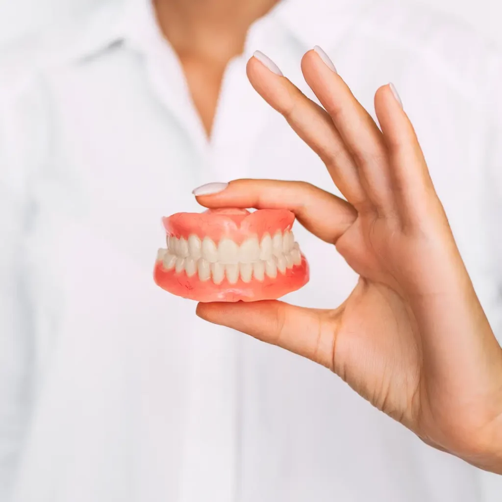 Mano della dentista che mostra dentiera mobile